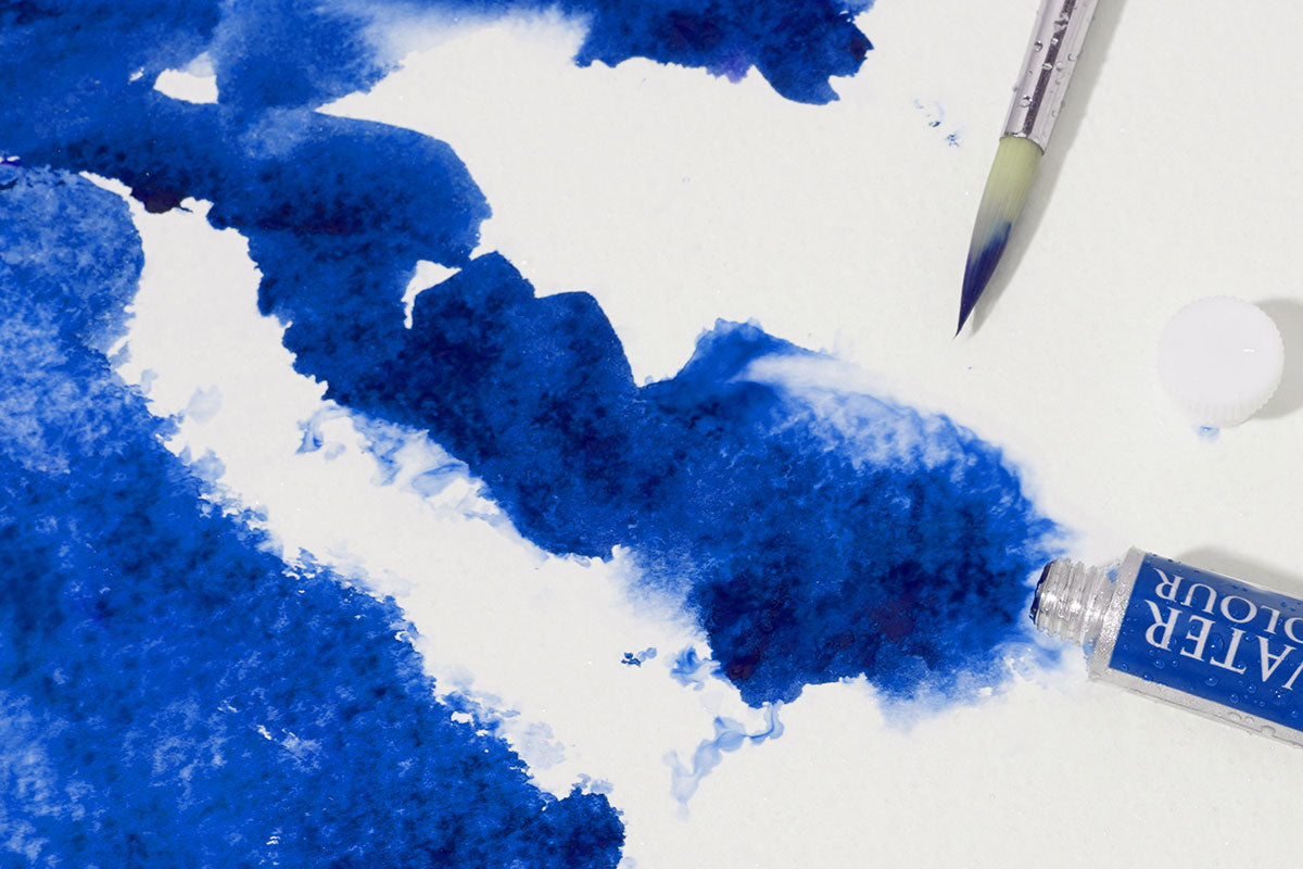 A blue tube of watercolor paint, and a watercolor brush dipped in watercolor